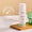 A white bottle of Green People Day Solution Cream SPF15 stands on a wooden tray beside a ribbed green glass vessel.