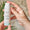 Hands holding a bottle of Green People Firming Face & Neck Serum with a Dermatologically Tested seal overlay.