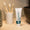 A white tube of toothpaste with a green label stands upright on a wooden counter next to three bamboo toothbrushes.
