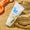 White SPF50 sun cream tube on sand next to an orange plastic spade, with the bottom left corner cut off.