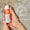 Hands holding an orange and white bottle of Oy Clear Skin Cleansing Moisturiser with a Dermatologically Tested badge.